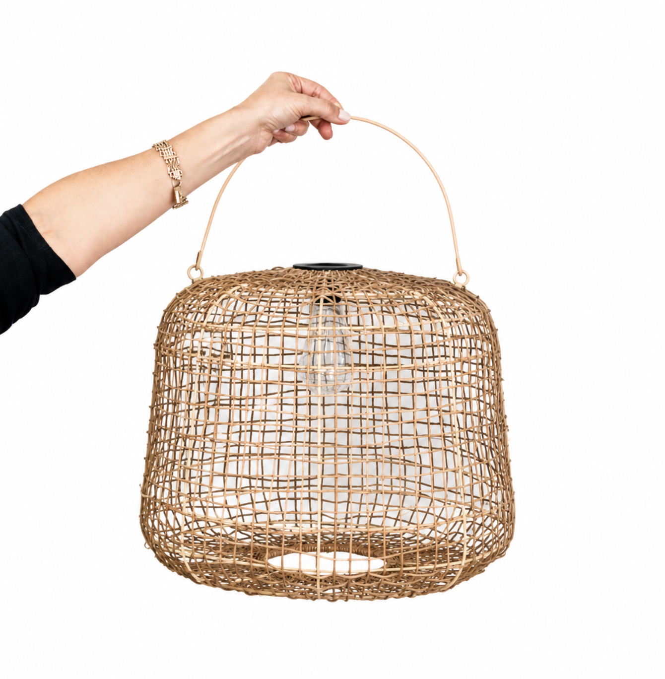 A hand holding the handle of a woven rattan pendant light against a solid white background.