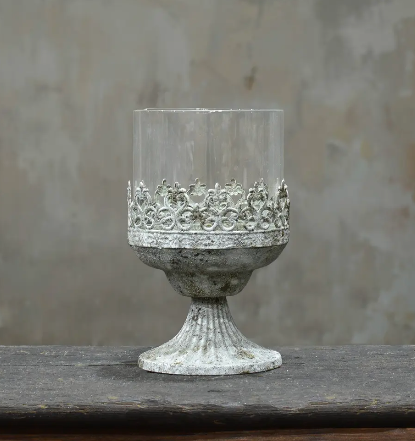 Large footed metal crown candle holder with pierced fleur-de-lis band and glass hurricane insert in aged Blanca patina
