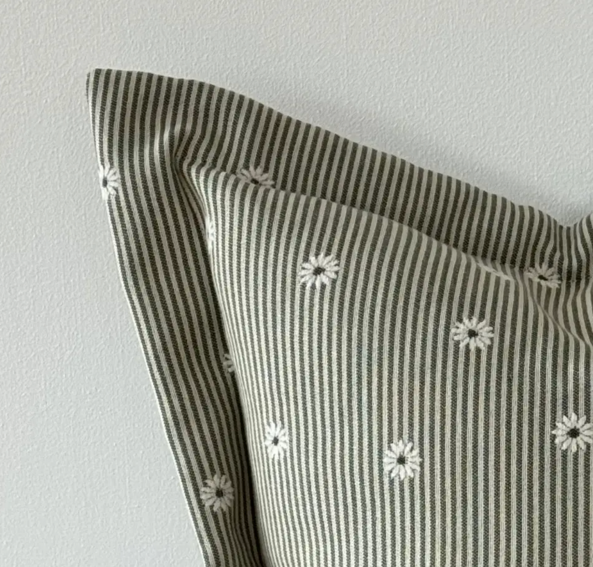 Close-up of sage and cream striped fabric, daisy pattern and flanged edge on a square cushion cover