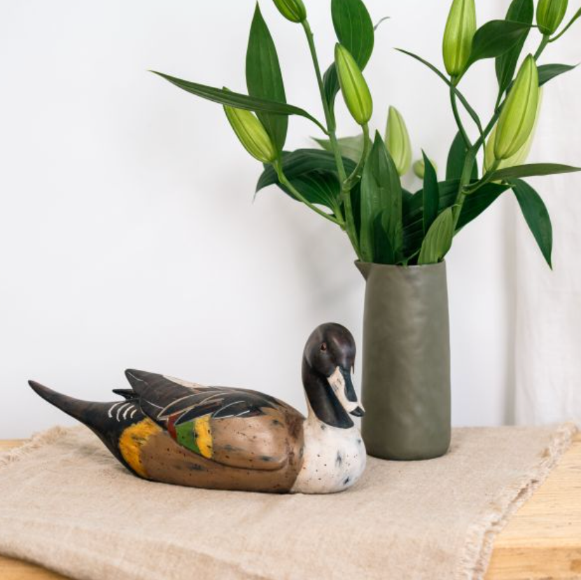Large seated duck sculpture with dark head, pale chest and patterned brown wings beside a vase