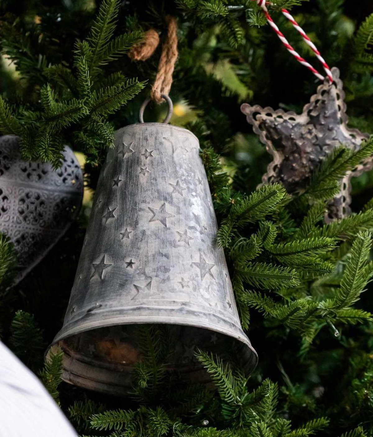 Close-up of star zinc bell hanging beside a star ornament on Christmas greenery