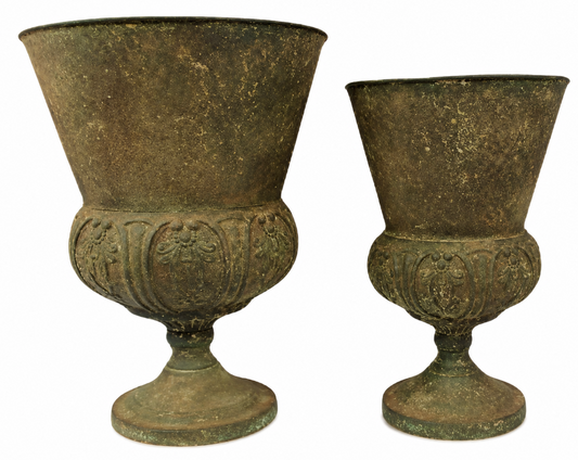 Two antique bronze pedestal cups with flared rims and ornate embossed floral details on the body, shown against a plain white background.