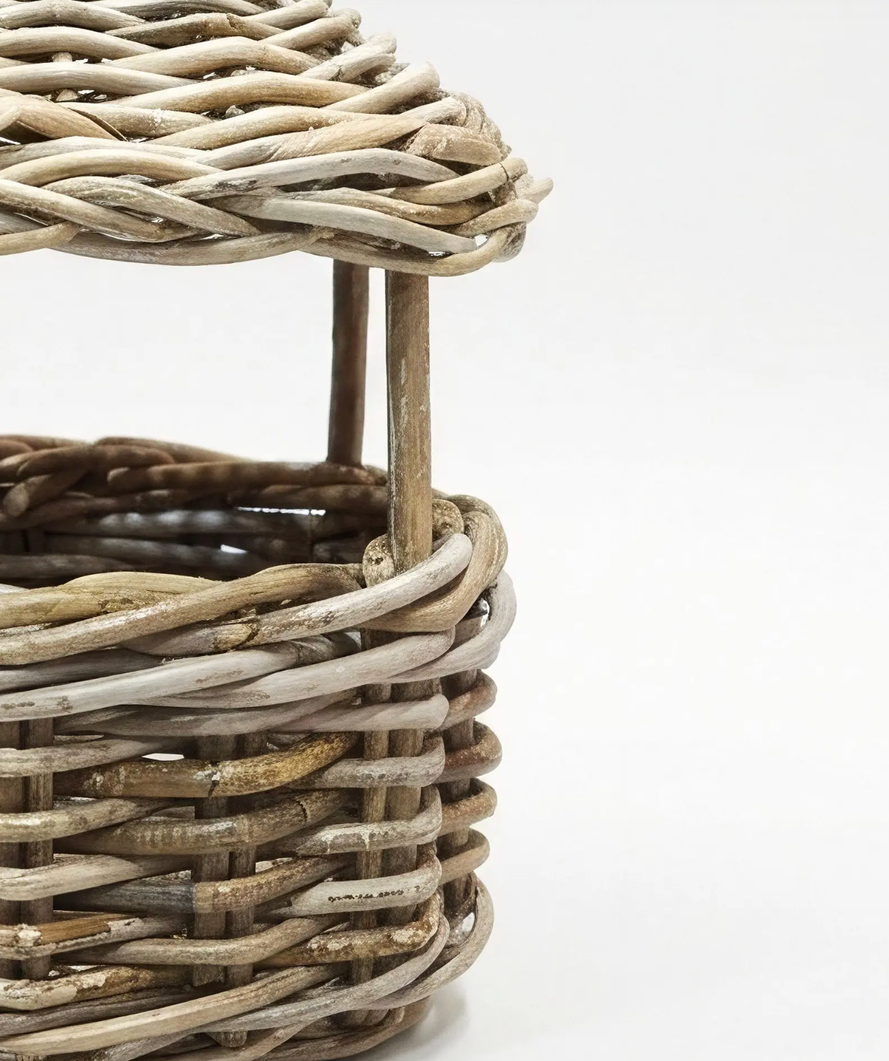 Close-up of a woven wicker basket with a matching lid, showing natural tan and light gray weathered wicker details on a white background.