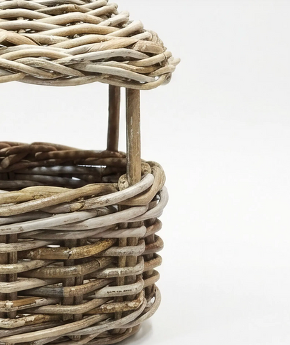 Close-up of a woven wicker basket with a matching lid, showing natural tan and light gray weathered wicker details on a white background.