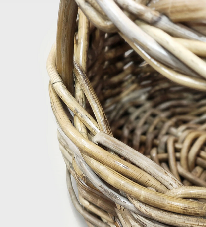 Close-up detail of a woven basket made from natural wicker or rattan, showing the interlaced strands and texture against a plain light background.