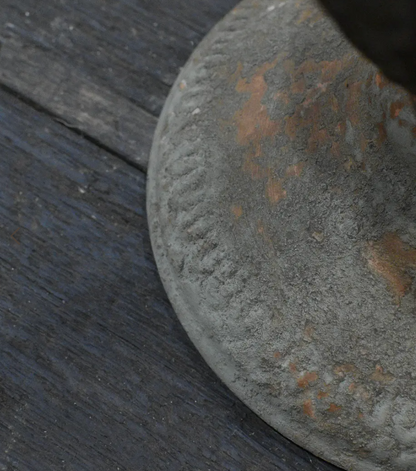 A close-up of a round, weathered gray metal object with rusted orange patches, resting on a dark wooden surface.