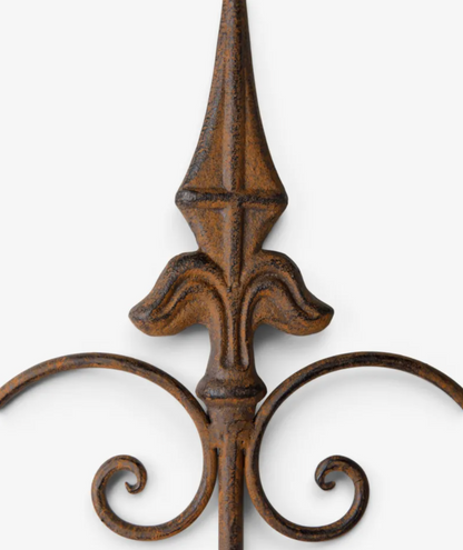 Close-up of a decorative wrought iron fence post with a textured, distressed brown finish and ornate scrollwork at the base, set against a plain light gray background.