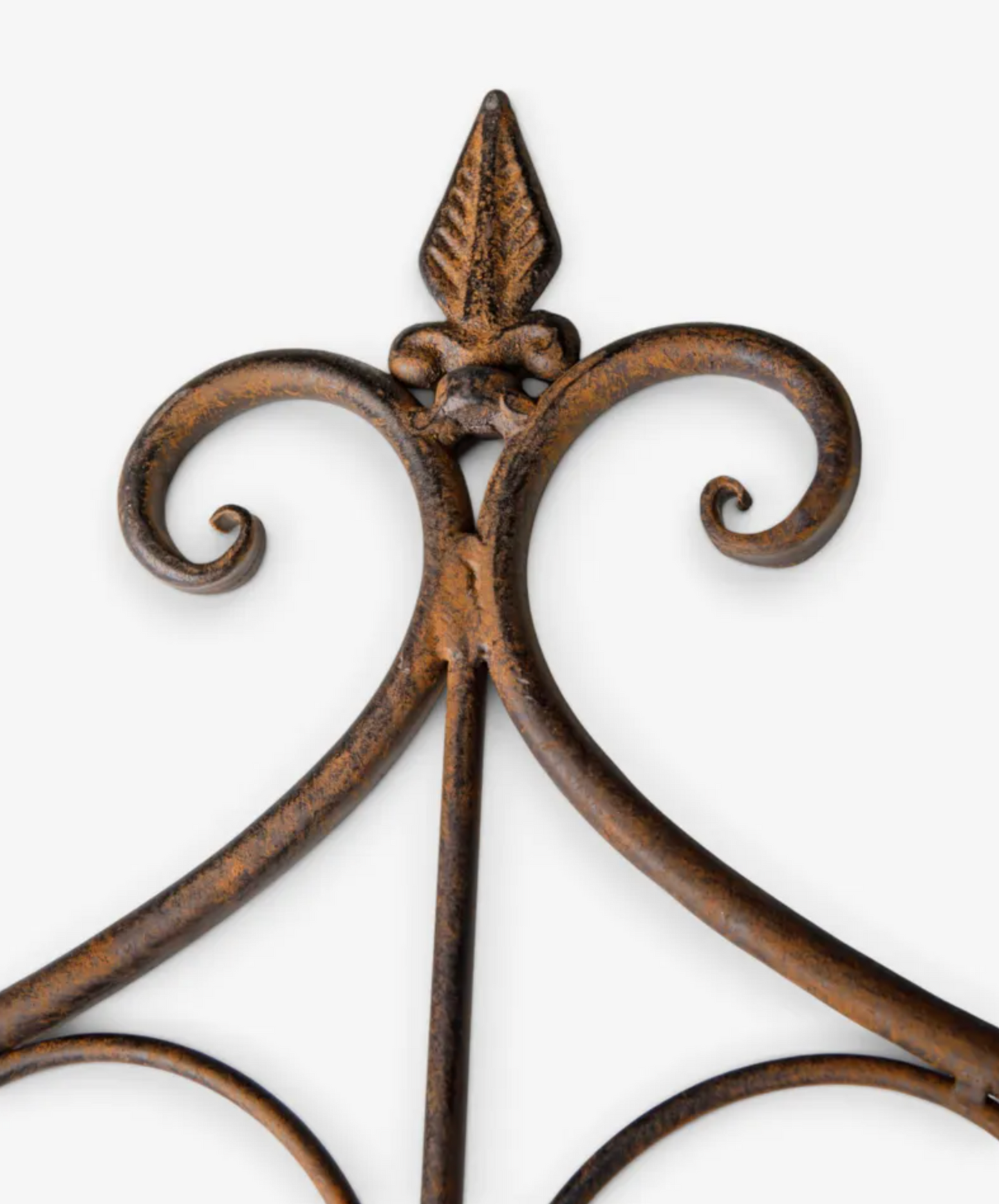 Close-up of a decorative wrought iron wall hanging with a distressed bronze-brown finish and scrolled arms on a light gray background.