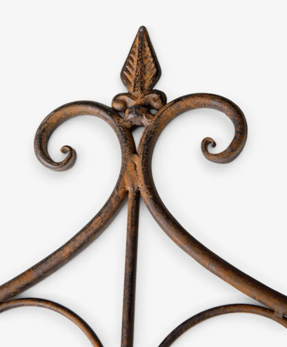 Close-up of a decorative wrought iron wall hanging with a distressed bronze-brown finish and scrolled arms on a light gray background.