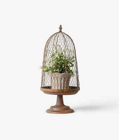 A rustic metal birdcage planter with a wooden pedestal base, holding a green potted plant in a textured beige pot, set against a plain white background.