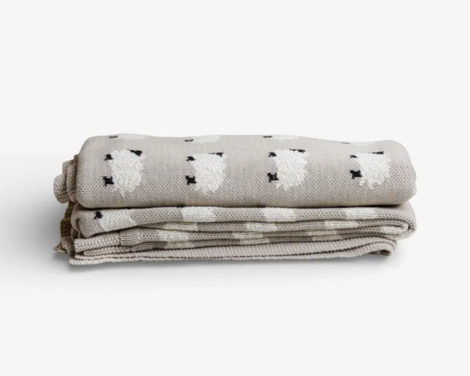 A folded woven blanket in a light oatmeal beige color, featuring a pattern of white sheep with small black accents, set against a clean white background.