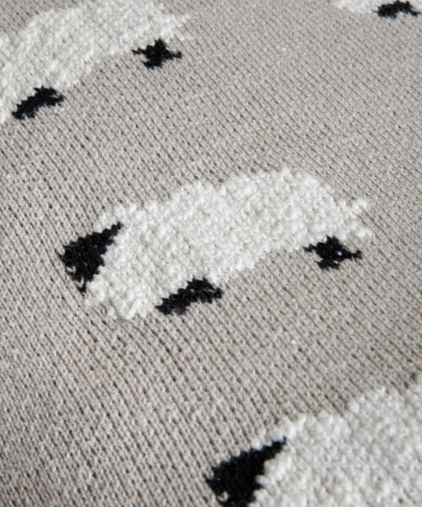Close-up of a textured knit fabric featuring stylized white sheep with black accents on a light beige background.