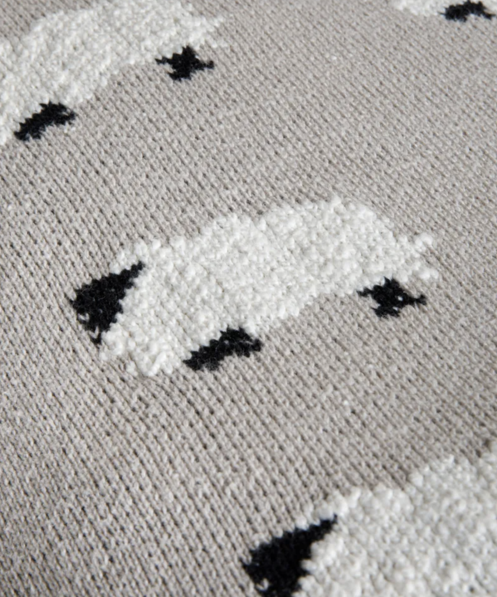 Close-up of a textured knit fabric featuring stylized white sheep with black accents on a light beige background.