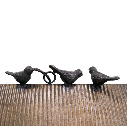 Three small cast iron bird ornaments in dark weathered finish perched on a wooden surface