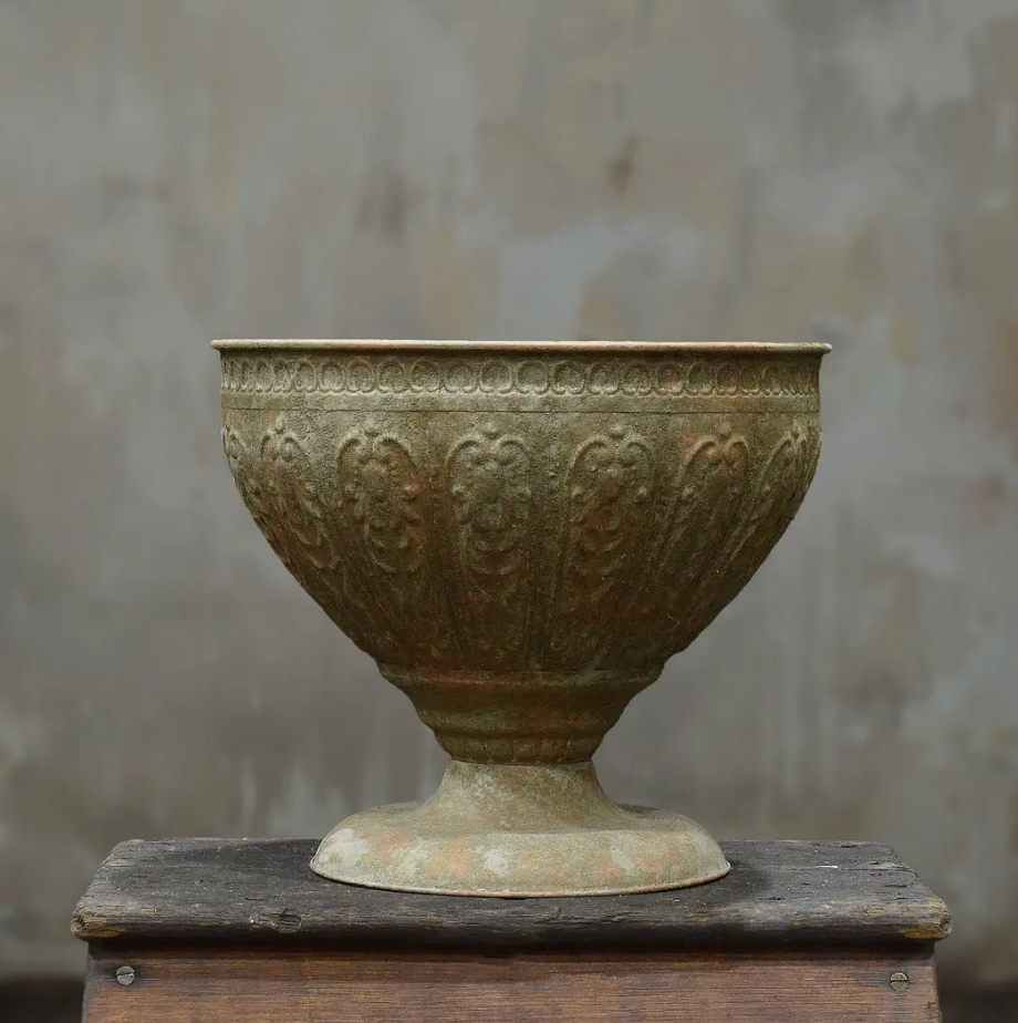 Large footed metal bowl with hand-embossed foliate motifs and beaded rim in aged Oxido patina on timber surface
