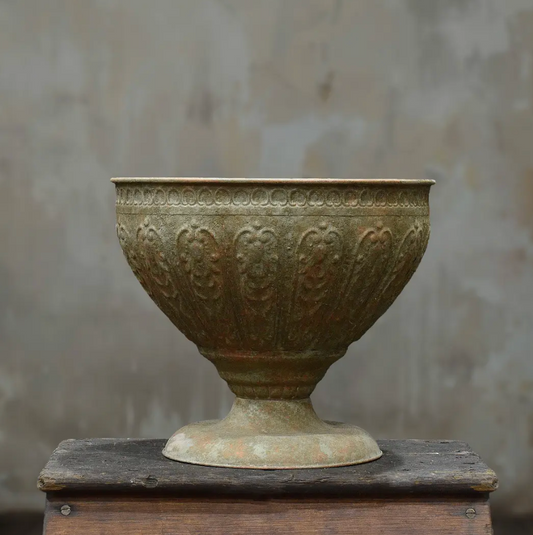 Large footed metal bowl with hand-embossed foliate motifs and beaded rim in aged Oxido patina on timber surface