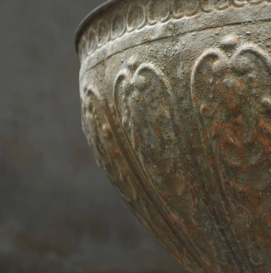 Close detail of embossed body and aged texture on large footed metal bowl showing depth of patina finish