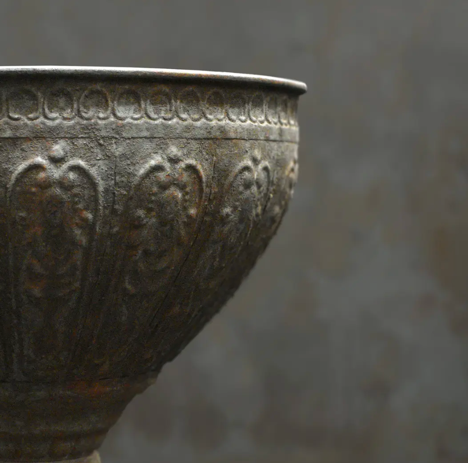 Close detail of hand-embossed foliate surface and beaded rim on large footed metal bowl in dark aged patina