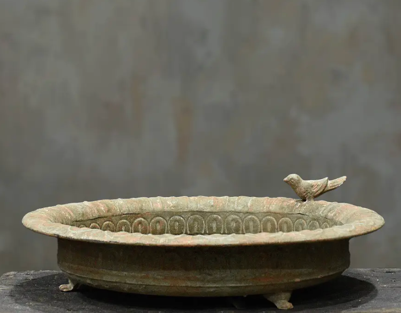 Close detail of cast iron bird perched on scalloped rim of aged bird dish