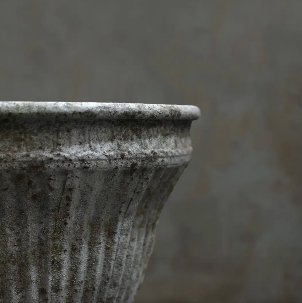 Close detail of scrollwork band below rim on fluted planter in aged white patina showing pitted texture