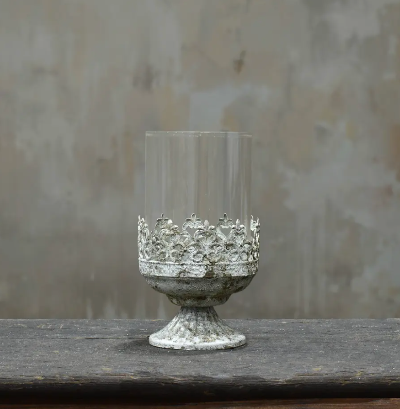 Small footed metal crown candle holder with pierced fleur-de-lis band and glass hurricane insert in aged Blanca patina