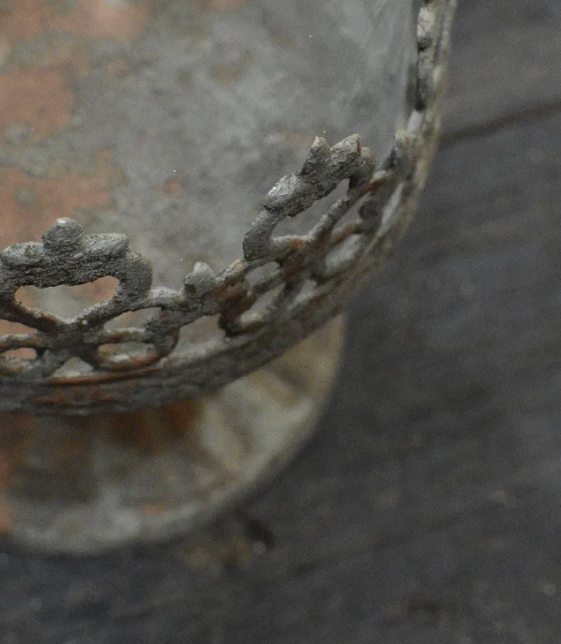 Close detail of pierced fleur-de-lis crown band on metal candle holder in aged patina