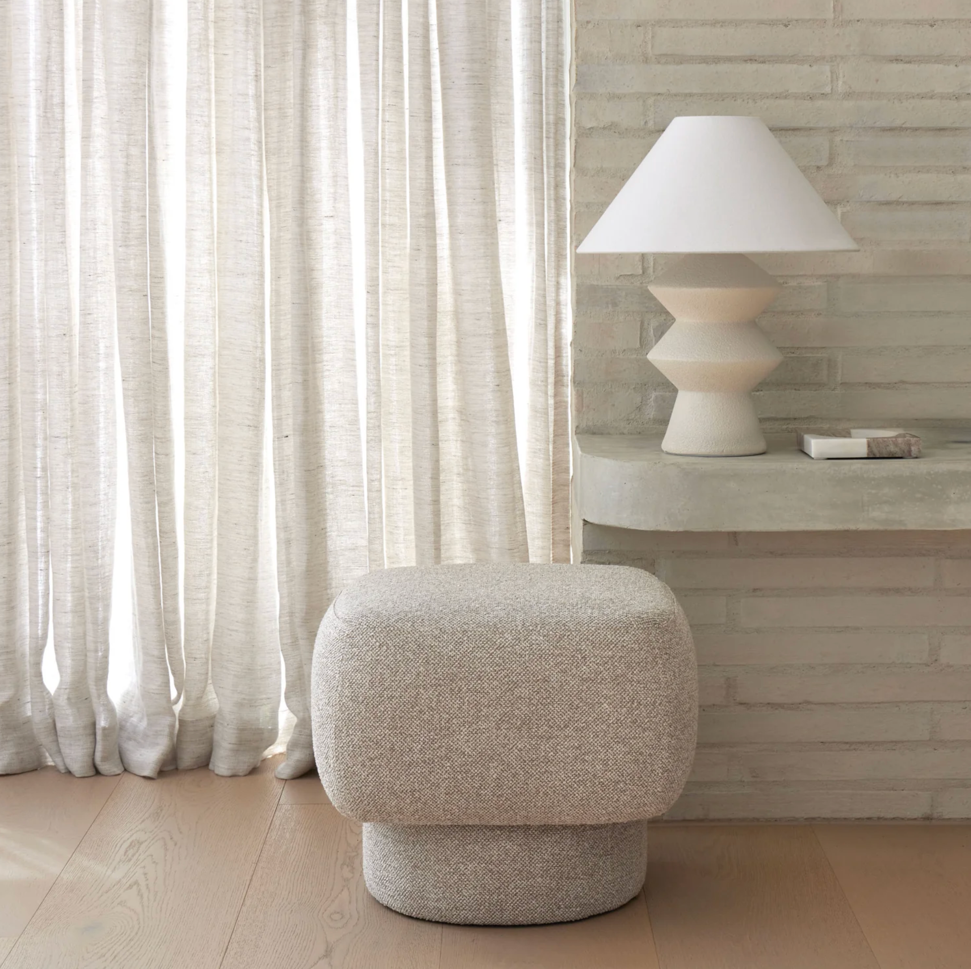 Geometric table lamp styled beside a boucle ottoman in a light-filled room