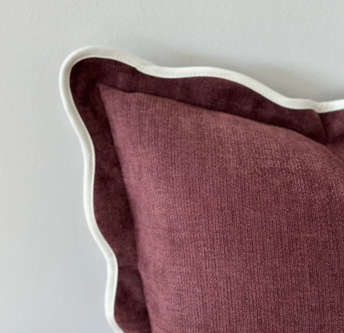 Close-up of plum textured fabric and scalloped edge on a square cushion cover