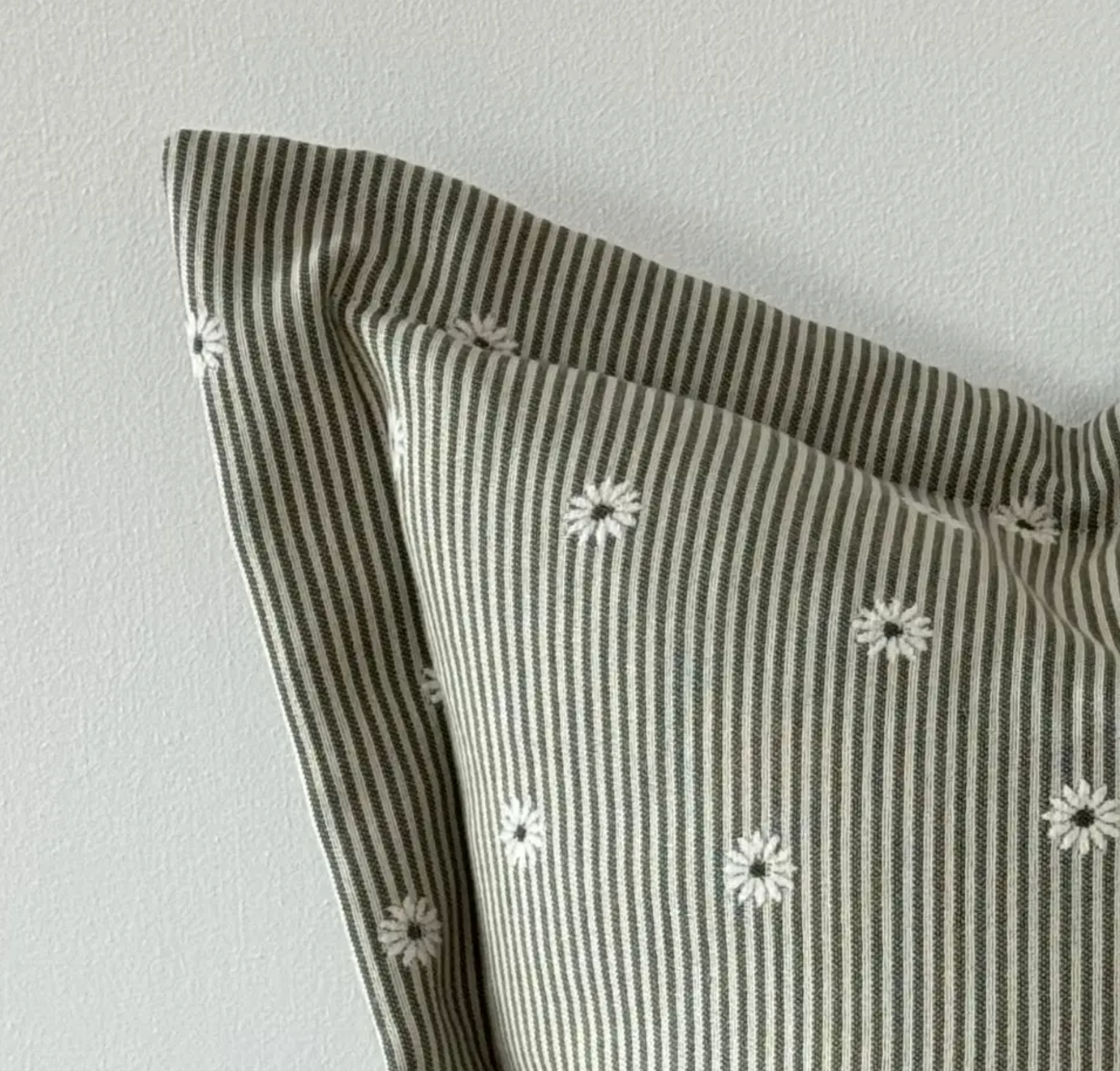 Close-up of sage and cream striped fabric, daisy pattern and flanged edge on a square cushion cover
