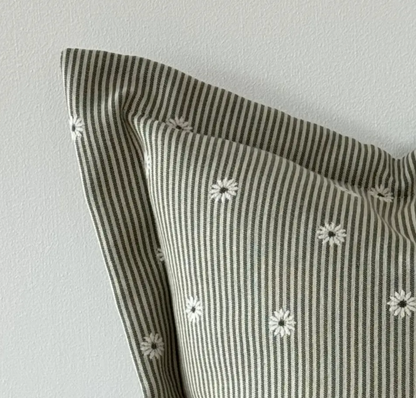 Close-up of sage and cream striped fabric, daisy pattern and flanged edge on a square cushion cover