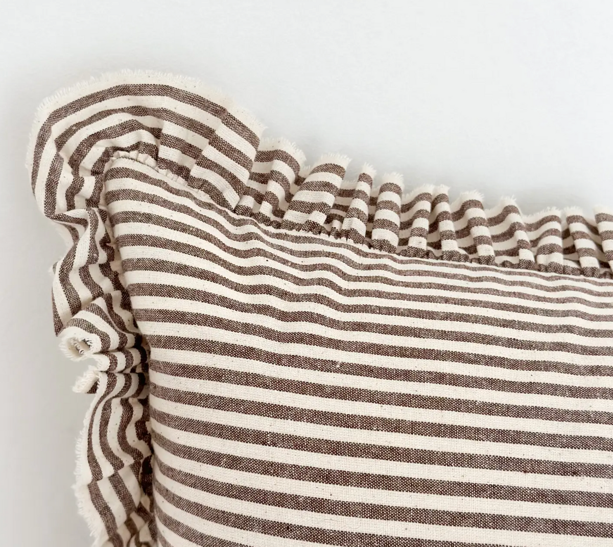 Close-up of dark brown striped cotton blend fabric and ruffled edge on a rectangular cushion cover