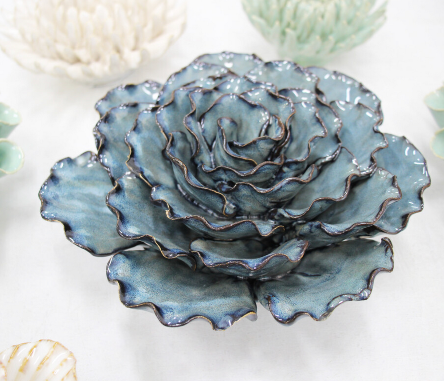 Side view of a large blue and teal ceramic ocean wall flower with gold-edged petals on a white background.