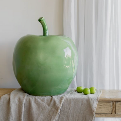 Large glossy green apple ornament with curved stem on a draped table