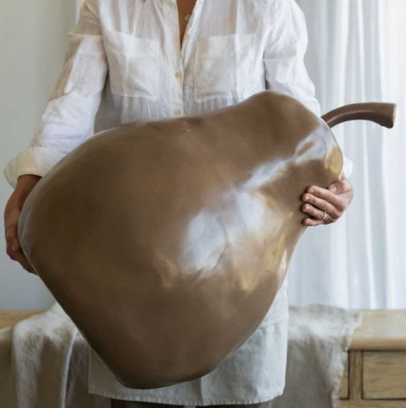 Large brown ceramic pear with curved stem displayed upright on a draped table