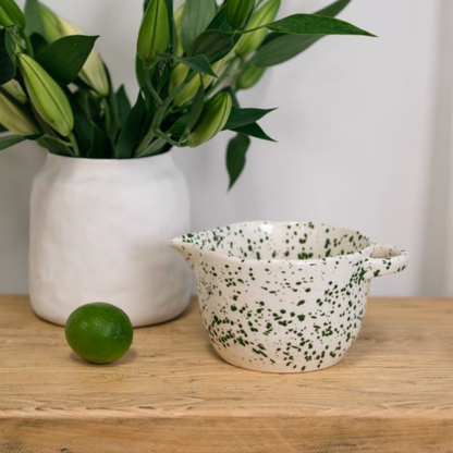 Green speckled pouring bowl beside a lime on a wooden table