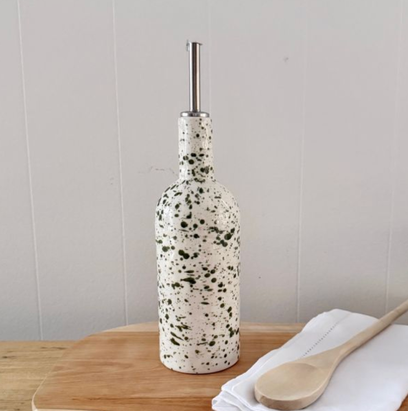 Tall white bottle with green splatter and metal pouring spout beside a wooden spoon