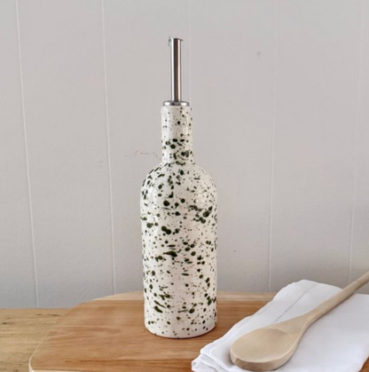 Tall white bottle with green splatter and metal pouring spout beside a wooden spoon