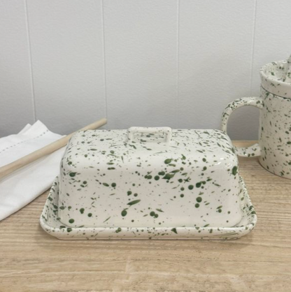 Green splatter butter dish with lid on a wooden table beside a matching jug