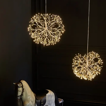 Two gold hanging dandelion lights with warm white LEDs against a dark wall
