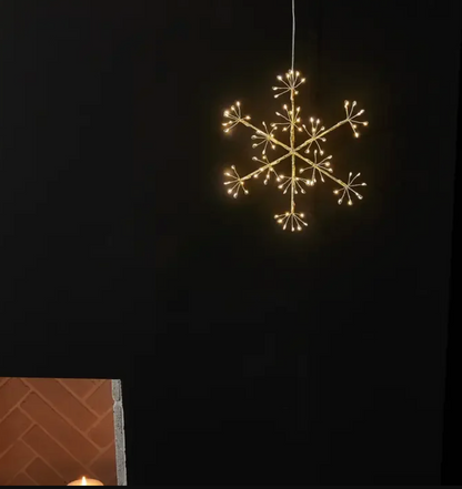 Glowing six-point snowflake hanging light against a pale wall