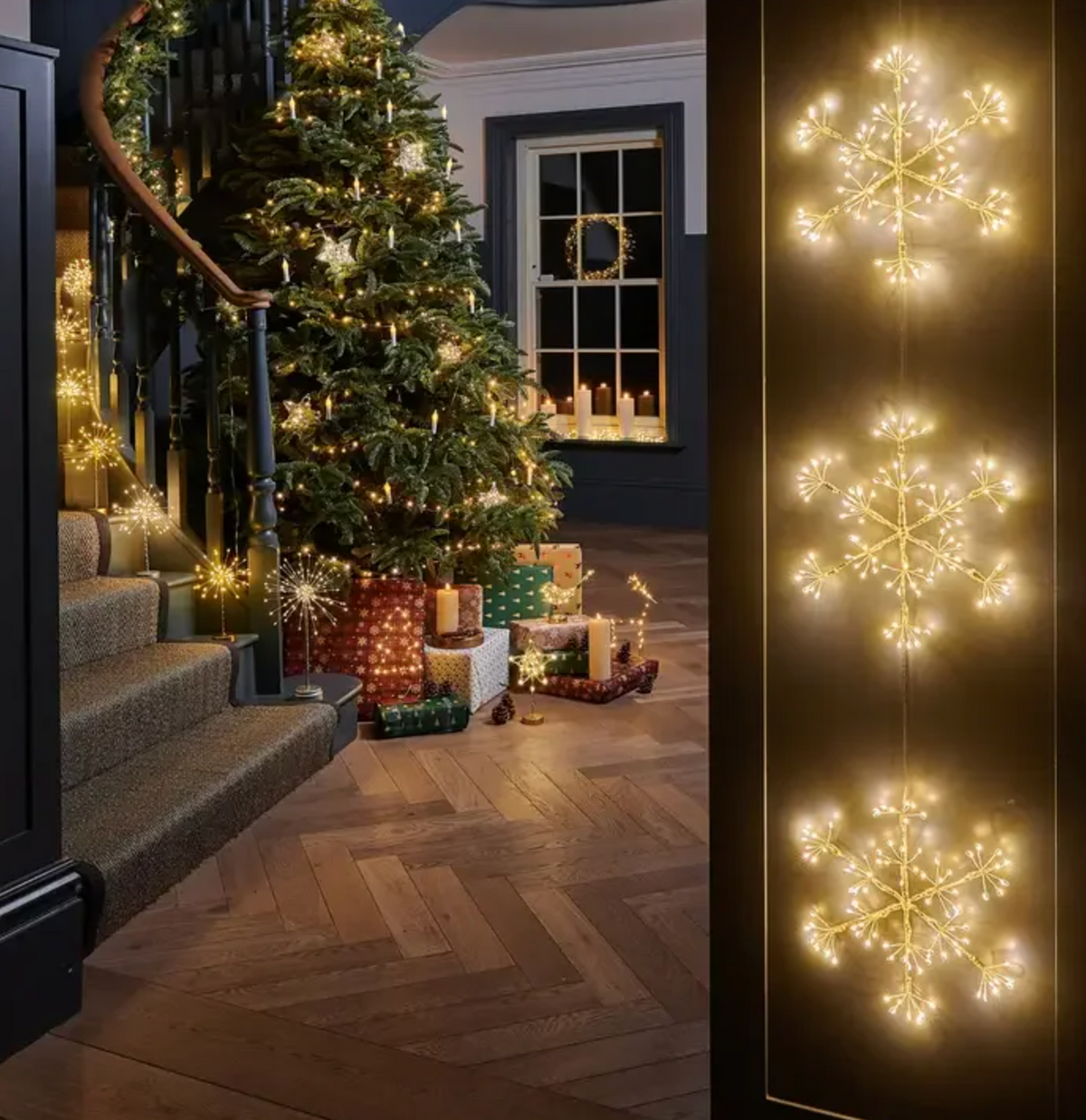 Three illuminated snowflake forms hanging vertically beside a decorated Christmas tree