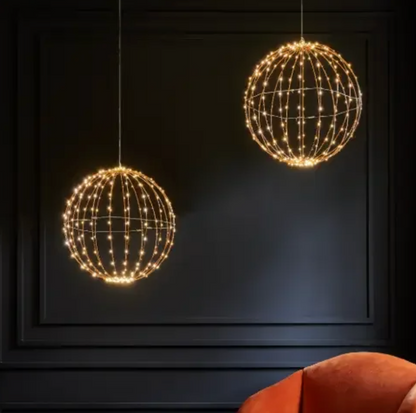 Two glowing open-frame sphere lights hanging against a dark wall