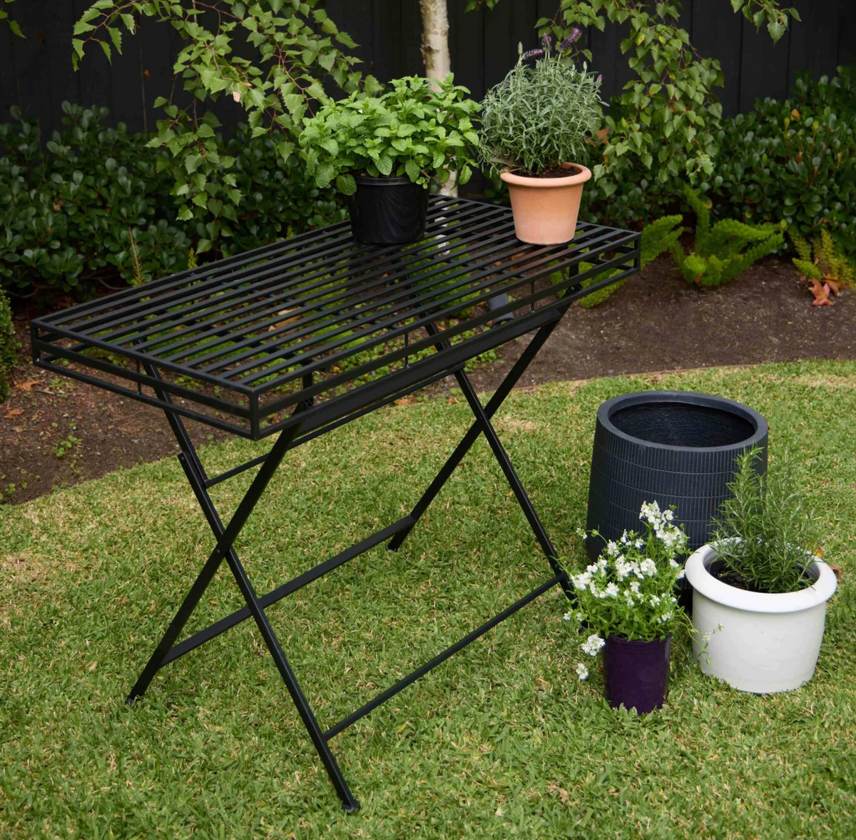 Black iron garden table outdoors with potted plants on its slatted top