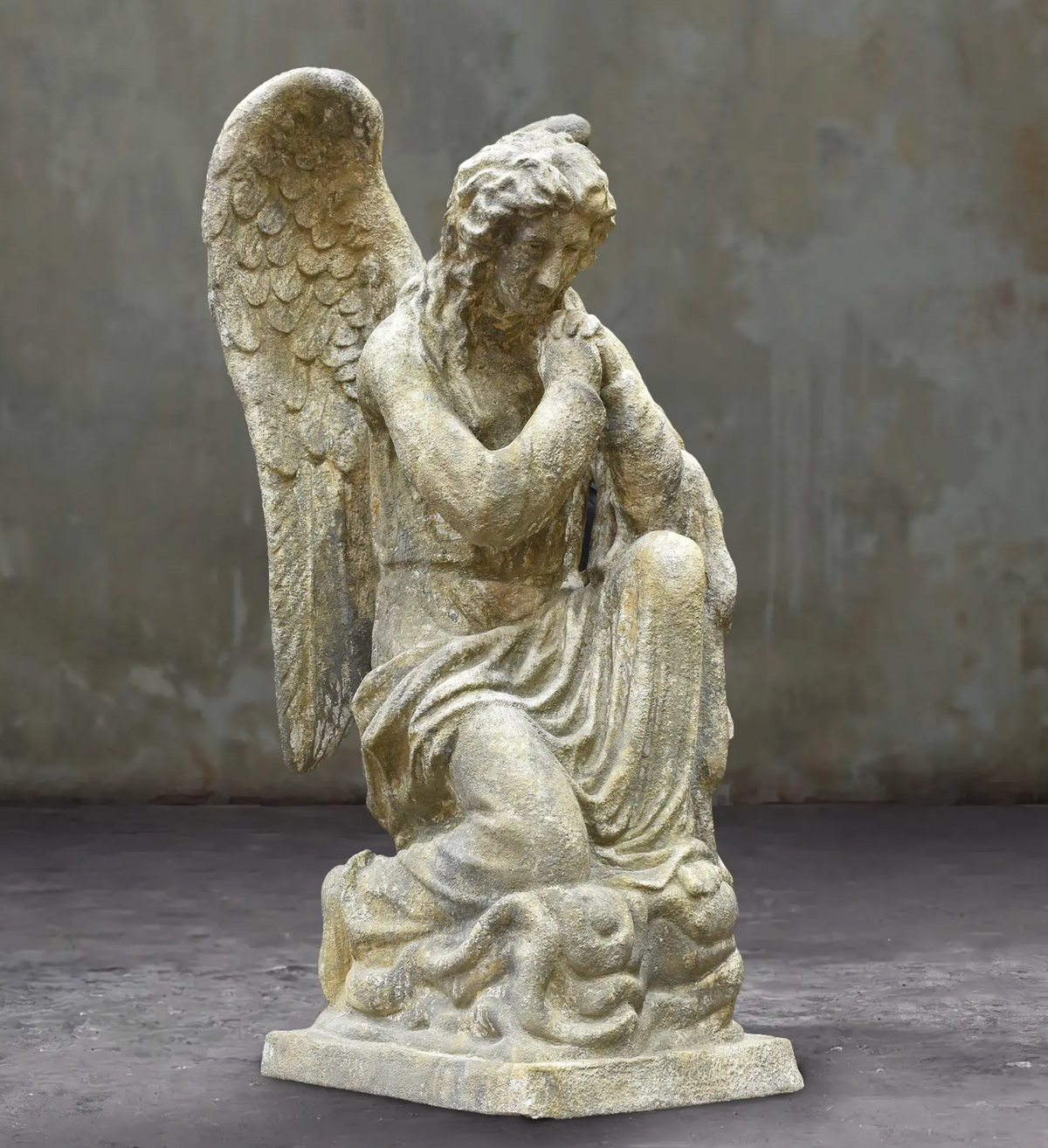 Kneeling angel statue with clasped hands, feathered wings and a weathered stone finish