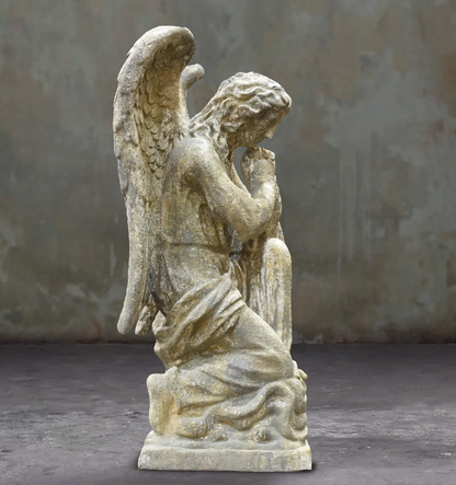 Side view of the kneeling angel statue showing bowed head and layered wing feathers