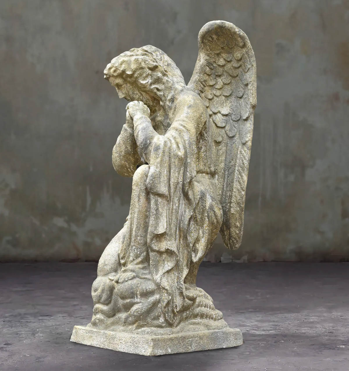 Angled view of the kneeling angel statue showing draped clothing and feathered wing