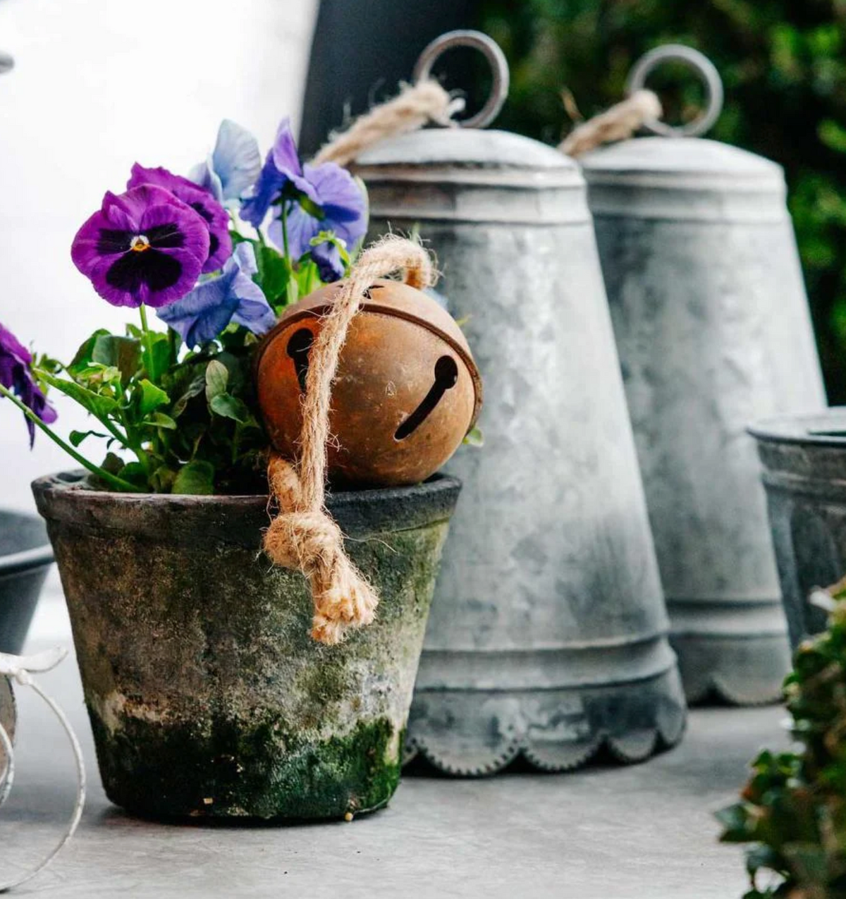 Scalloped zinc bells displayed beside a pot of purple flowers and a round bell