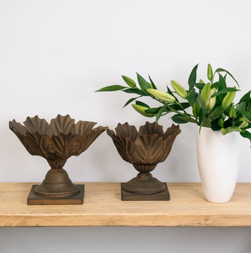 Two bronze rust-coloured acanthus leaf bowls with pedestal bases beside a white vase.