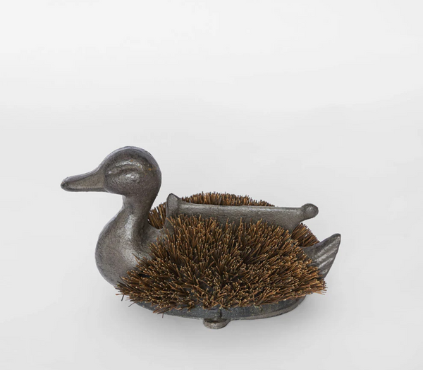Side view of a grey cast iron duck boot brush with brown bristles and a raised bar across its back.