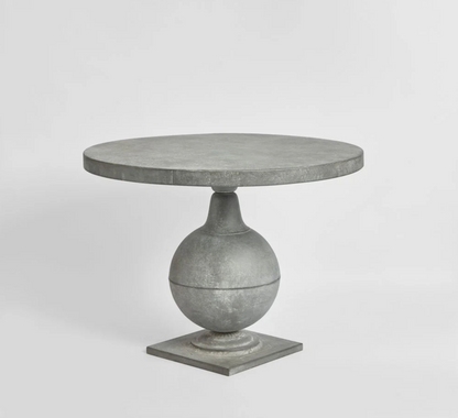Zinc finish pedestal table viewed at an angle, showing the round top and square base